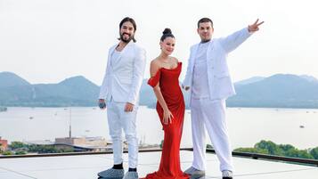 Three people standing on a reflective surface with a body of water and mountains in the background.