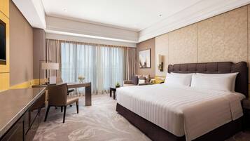 A hotel room with a large bed, a desk with a chair, a television, and a window with curtains.