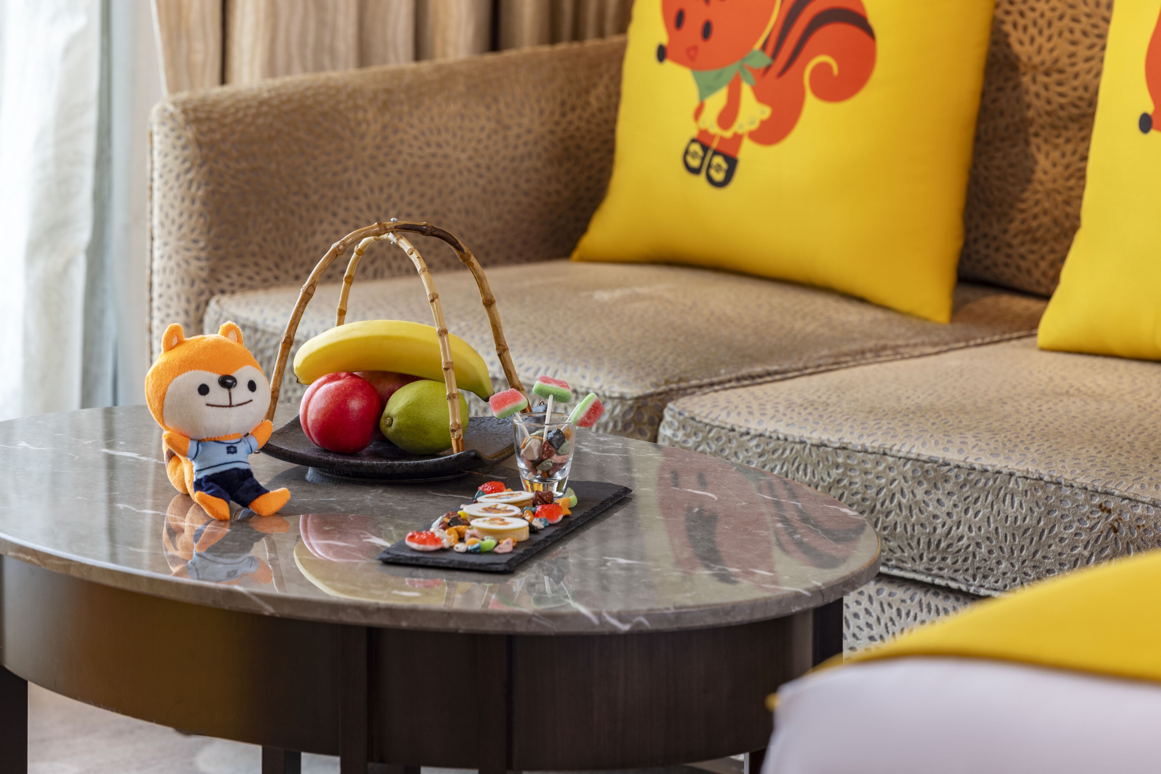 A round table with a plush toy, a fruit basket, and a tray of snacks.
