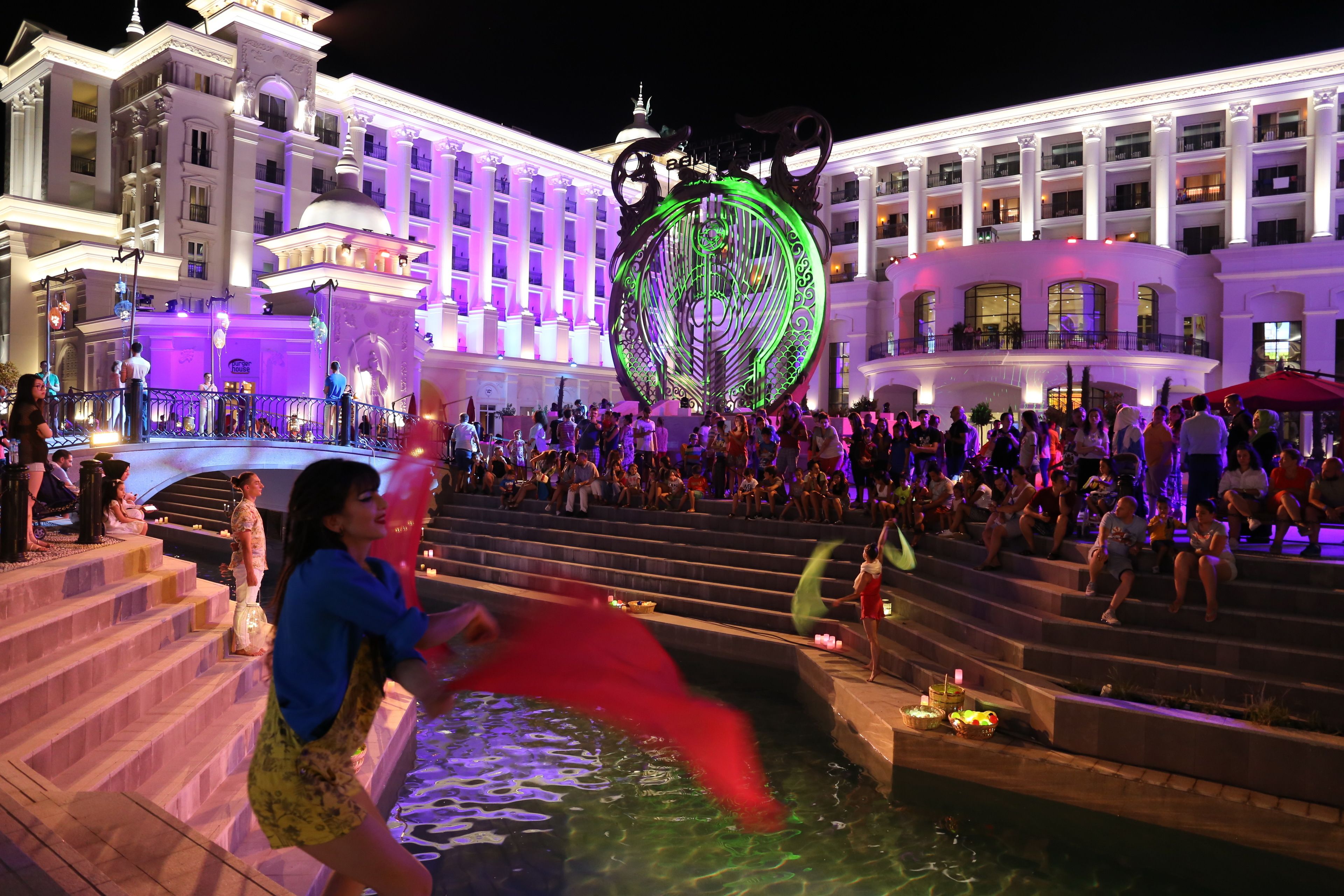A large, illuminated globe sculpture in front of a hotel with multiple balconies and a pool area.