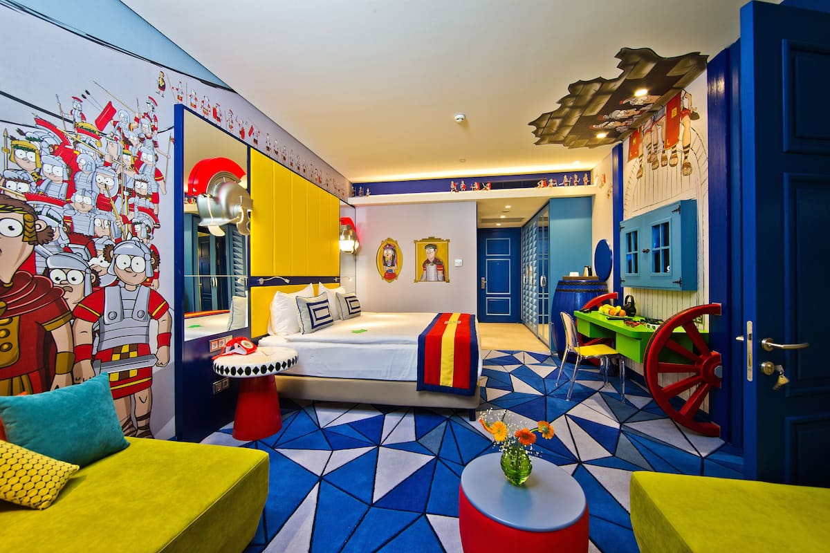 Ein Zimmer mit einem Bett, einem Schreibtisch und einem Stuhl. Eine Wand zeigt ein Wandgemälde und eine Tür hat einen Griff.