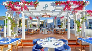 An outdoor dining area with white pergolas, blue chairs, and tables set for dining. - The Land Of Legends Kingdom Hotel (Serik)