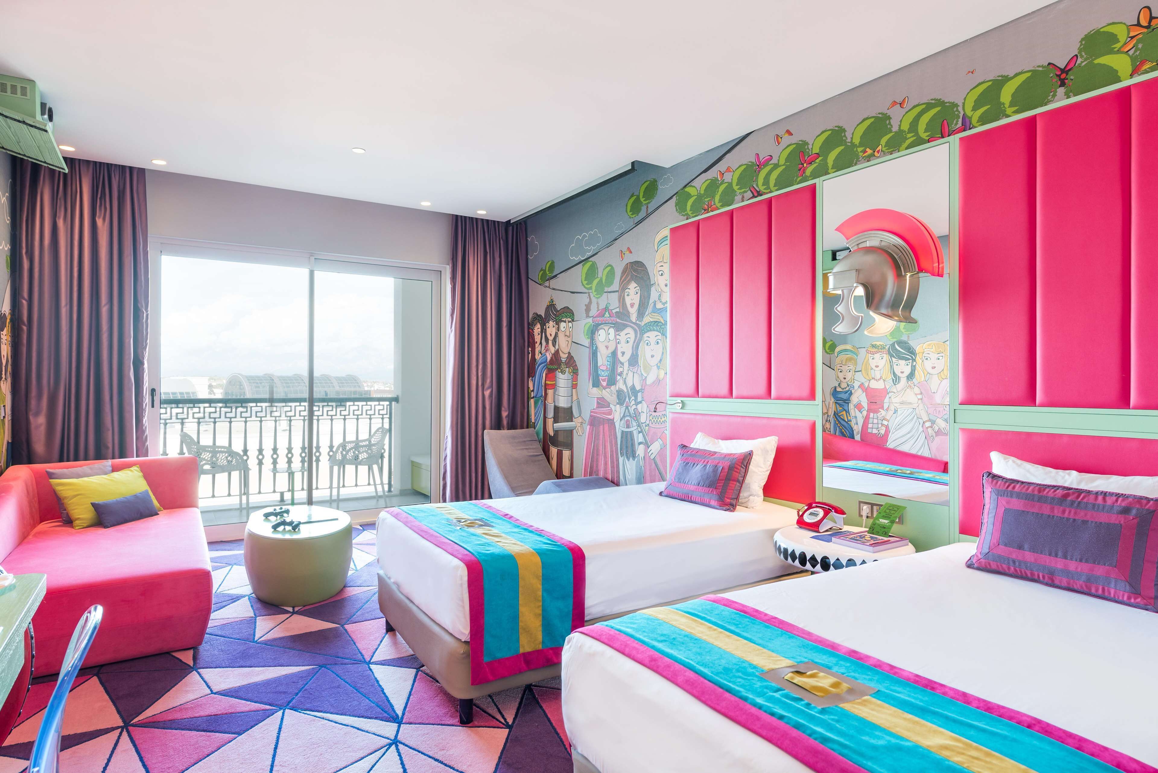 Een hotelkamer met twee bedden, een bank, een klein rond tafeltje en een balkon met uitzicht.