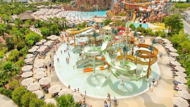 A water park with multiple slides and pools, surrounded by palm trees and beach umbrellas. - The Land Of Legends Kingdom Hotel (Serik)