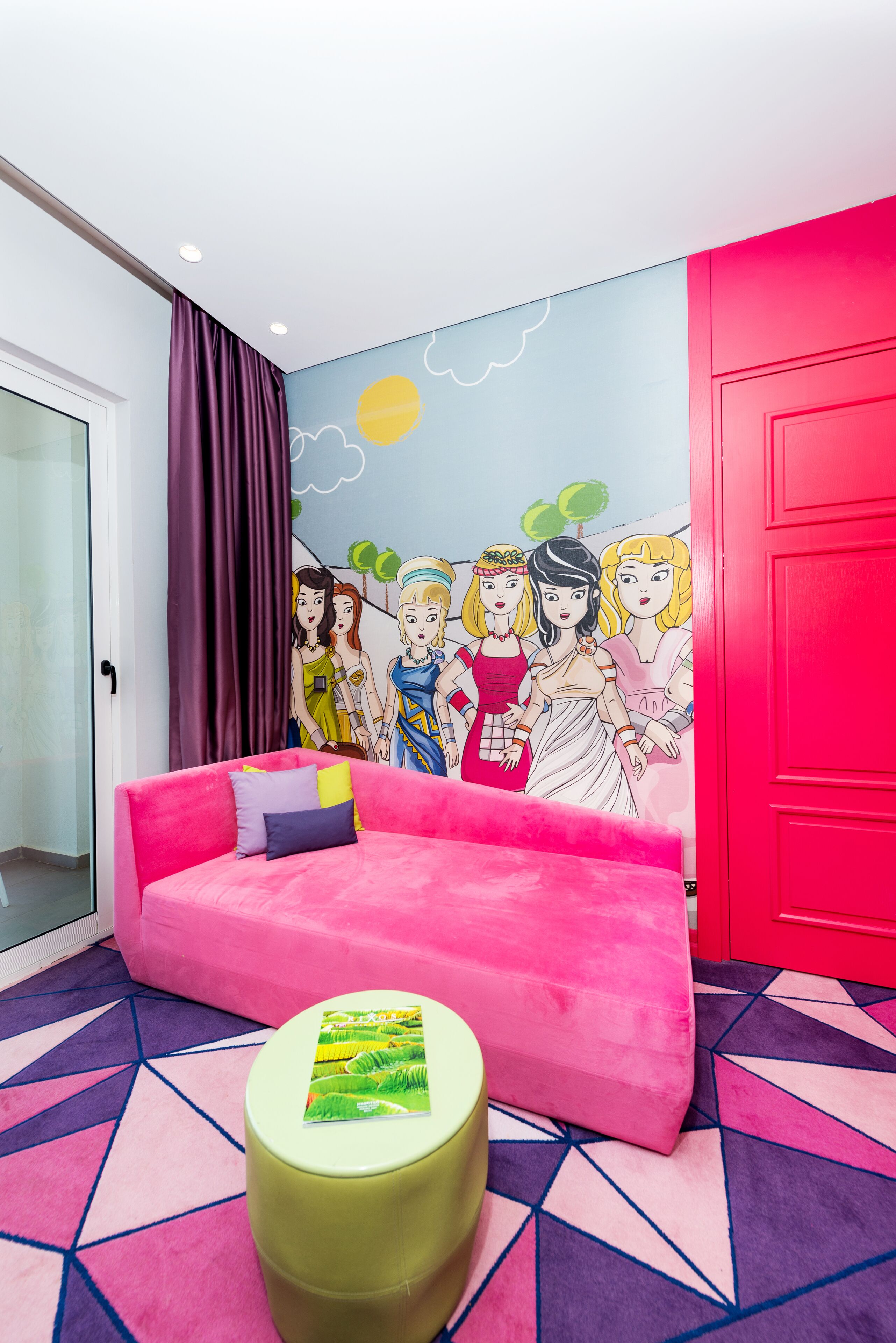 A vibrant room with a pink sofa, a green ottoman, and a colorful mural on the wall.