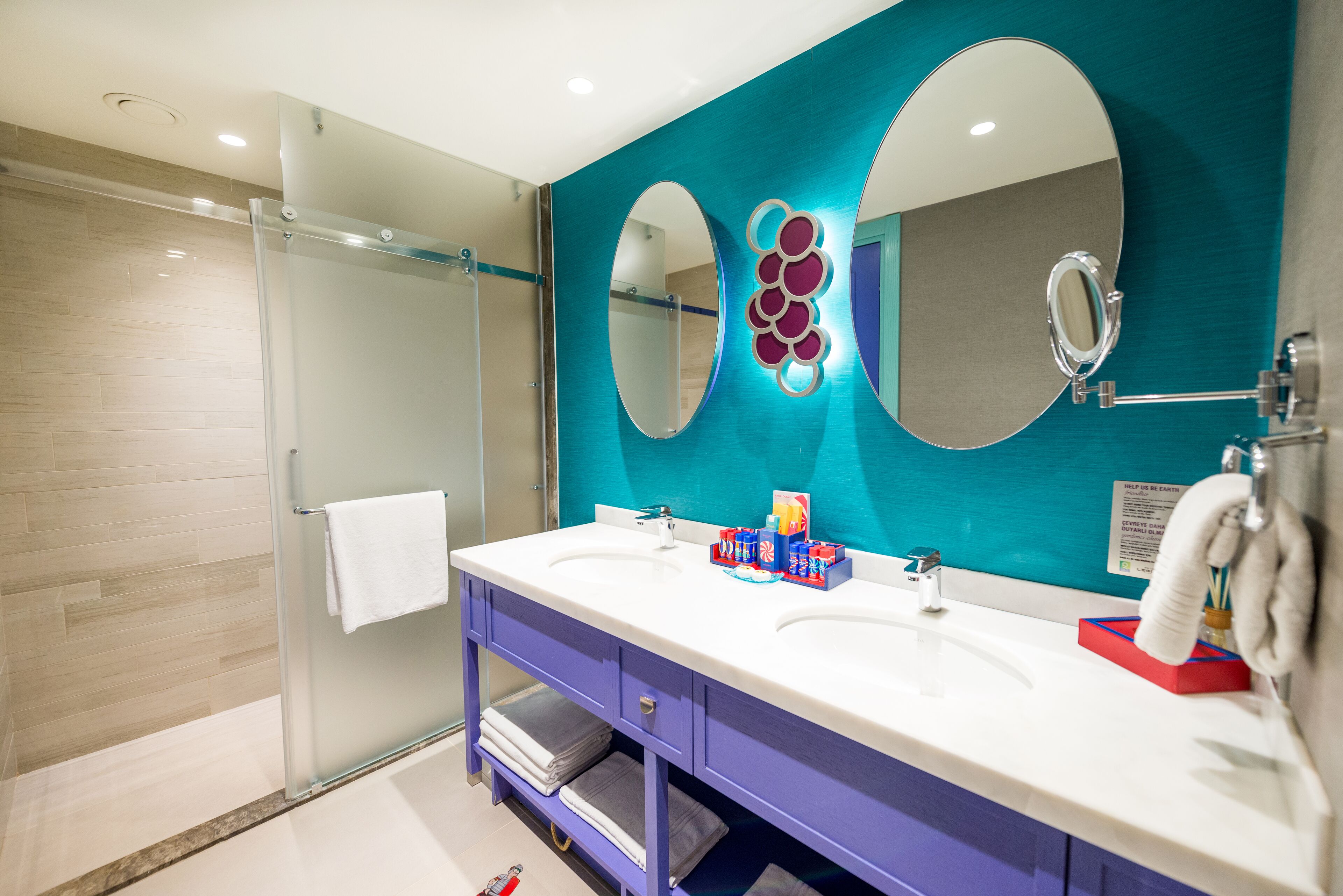 A modern bathroom with two sinks, a glass shower enclosure, and a teal accent wall.