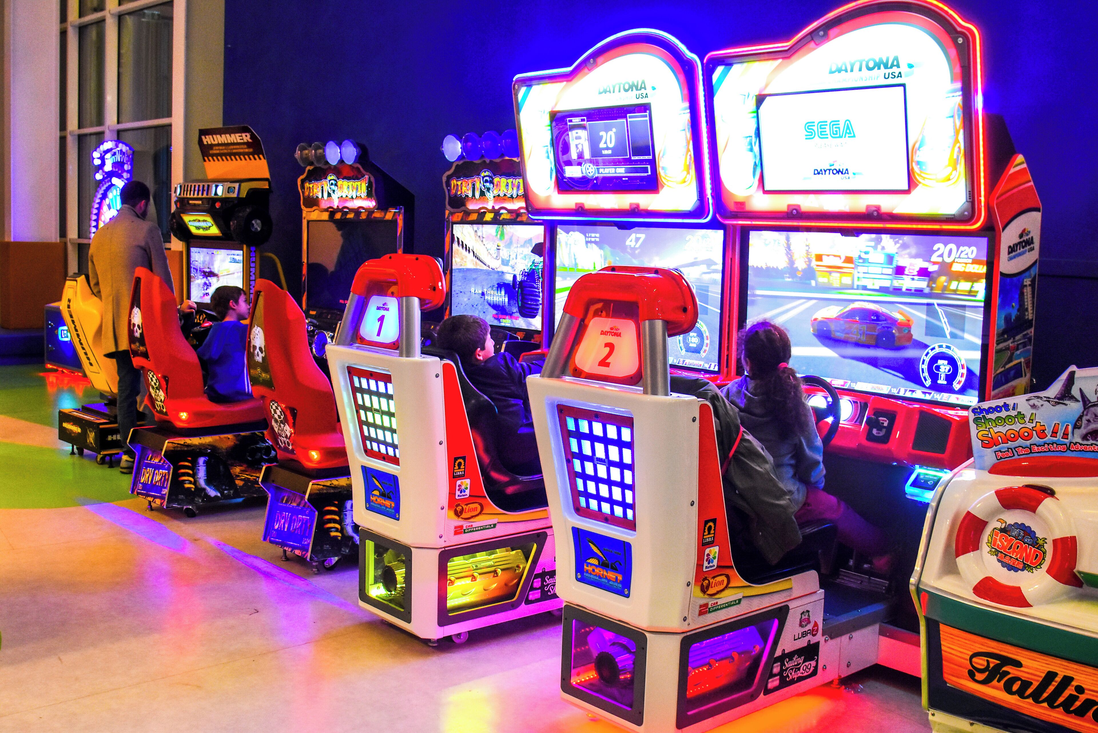 Une rangée de bornes d’arcade proposant des jeux de course, avec des néons et des écrans affichant des jeux de course.