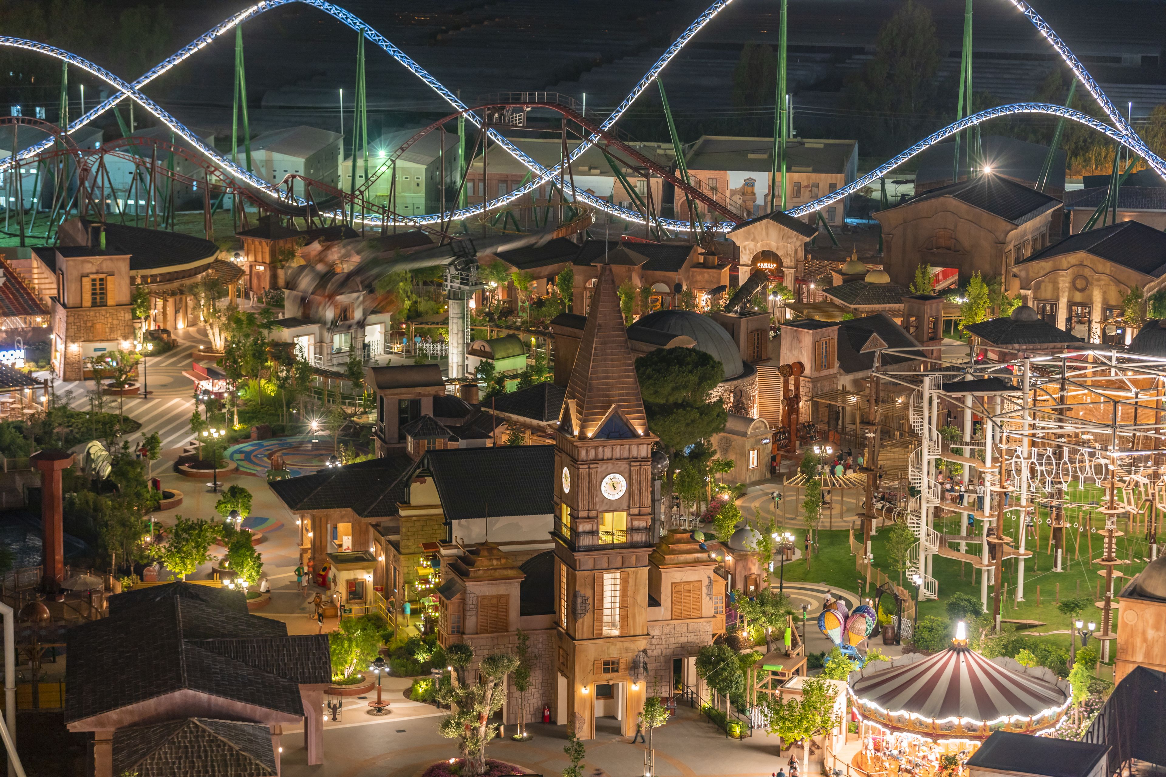 Une maquette d’un parc d’attractions à thème, comprenant différentes structures, notamment une tour de l’horloge, un carrousel et des pistes de montagnes russes.