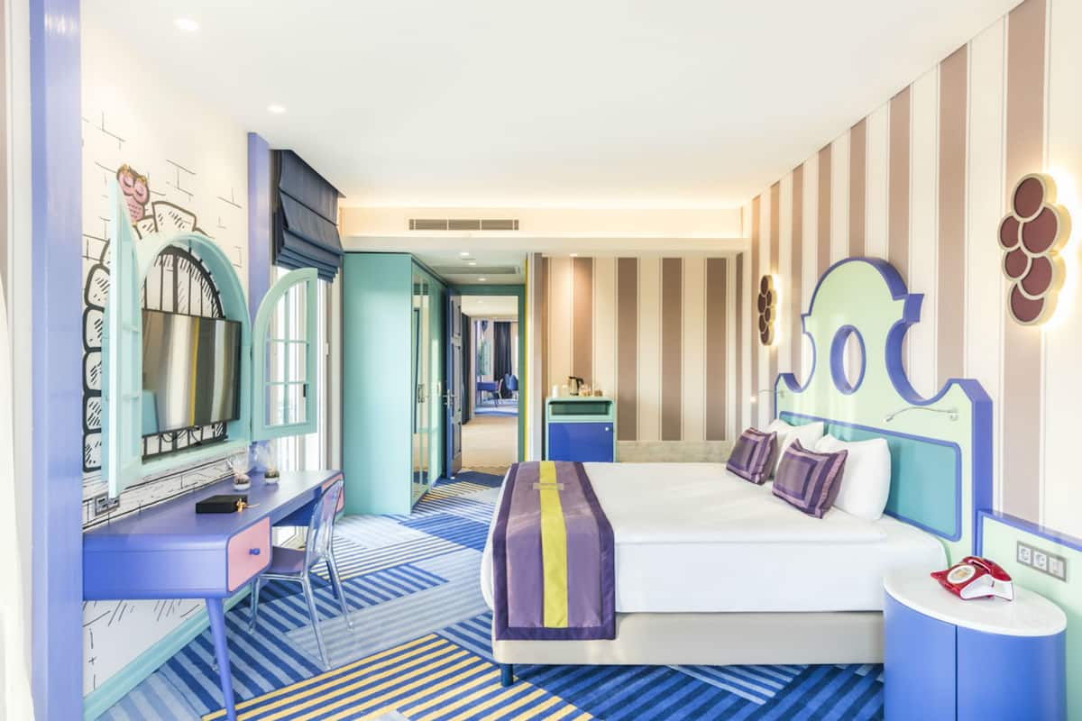 Ein Hotelzimmer mit Bett, Schreibtisch, Stuhl, Schminktisch mit Spiegel und einem durchgegangenen Tür erkennbaren Badezimmer.