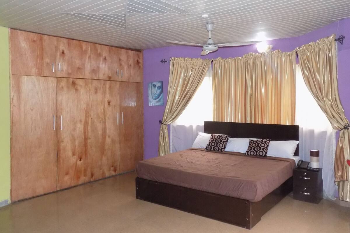 A bedroom with a bed, wardrobe, curtains, and a ceiling fan.