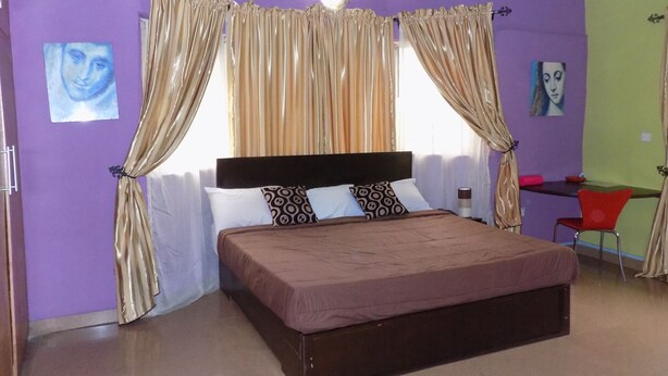 A bedroom with a bed, curtains, a ceiling fan, and artwork on the walls. - Posh Apartments Self Catering (Lagos)