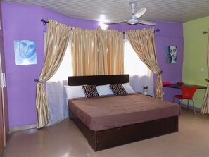 A bedroom with a bed, curtains, a ceiling fan, and artwork on the walls. - Posh Apartments Self Catering (Lagos)