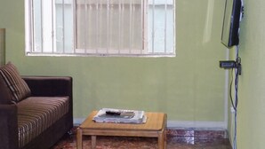 A living room with a sofa, a small wooden table, a window with metal bars, and a television mounted on the wall. - Posh Apartments Self Catering (Lagos)