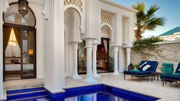 Un espace aménagé au bord de la piscine, avec une piscine aux carreaux bleus, des colonnes blanches et un coin salon équipé de chaises longues.