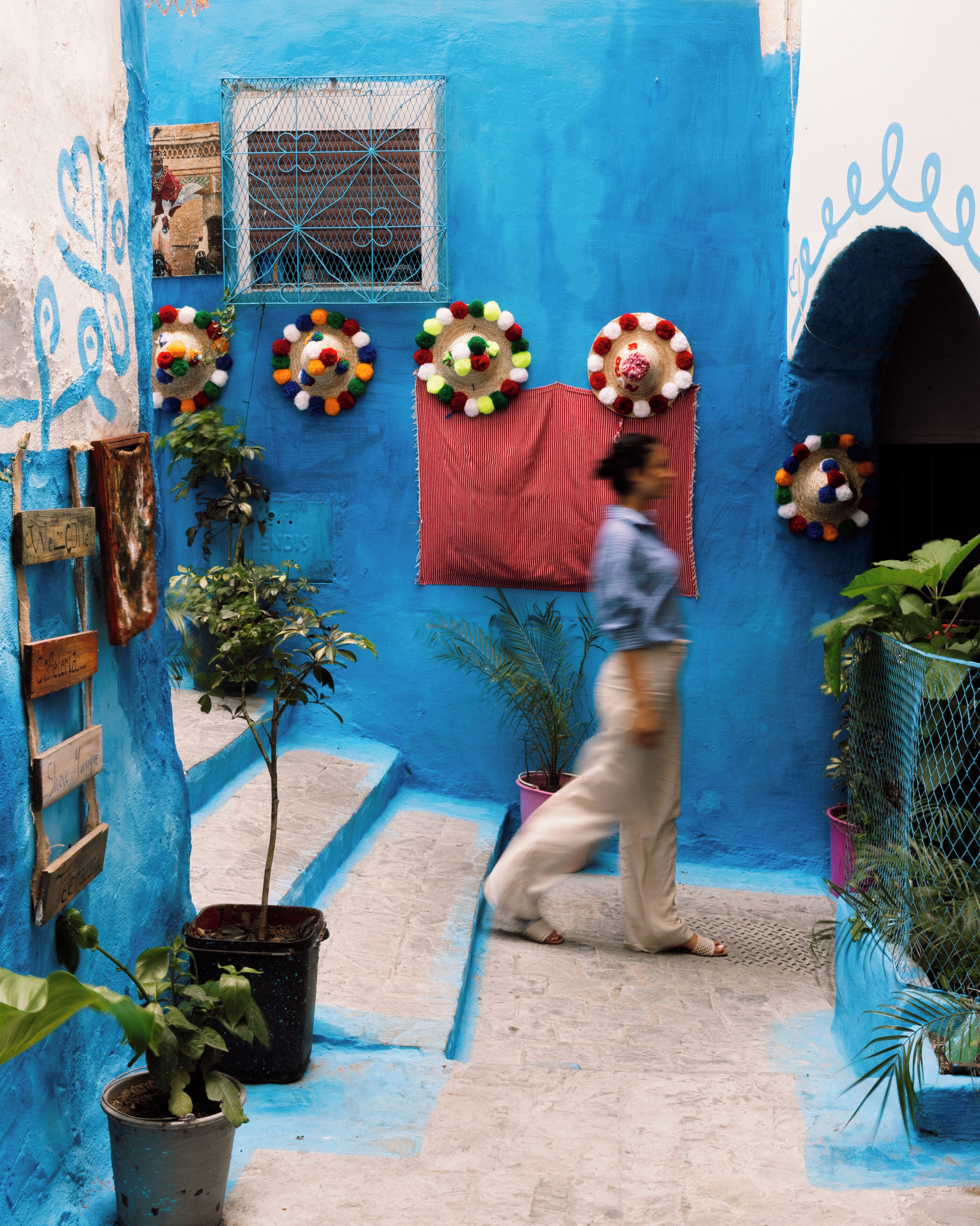 A narrow alleyway with a blue wall, a red cloth hanging, and potted plants.