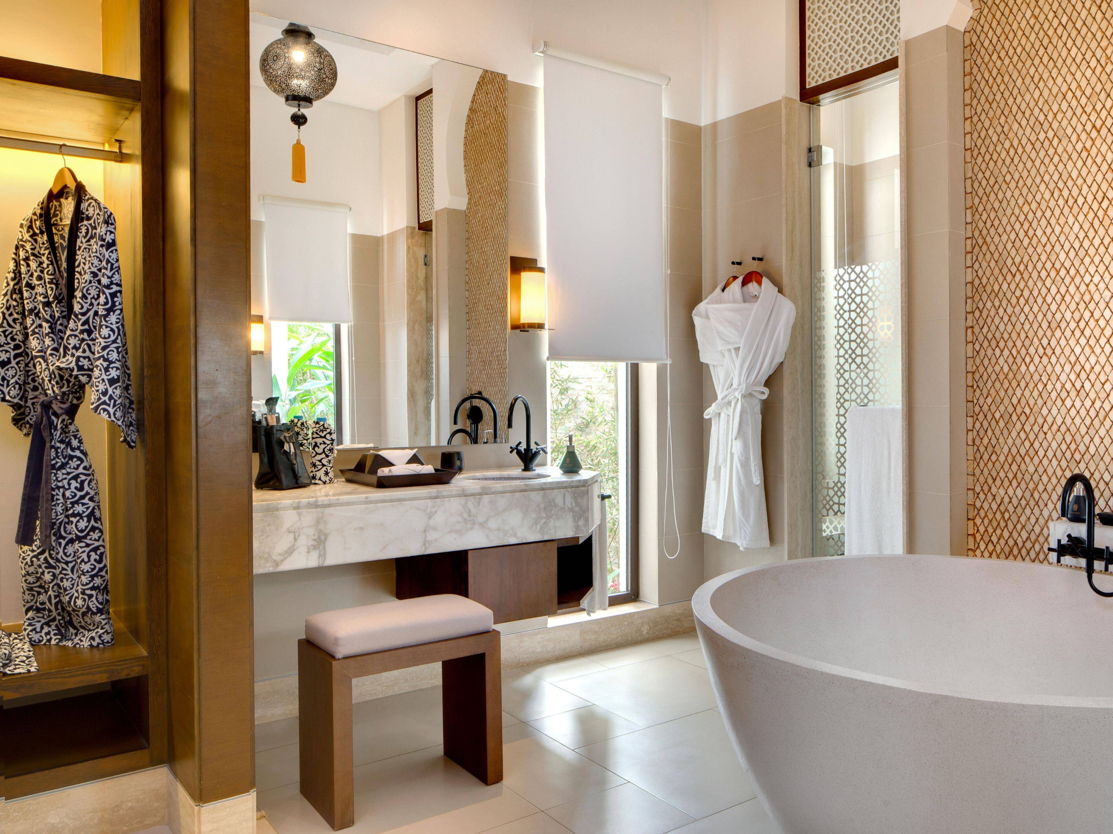 A modern bathroom with a large bathtub, a vanity with a mirror, and a robe hanging on the wall.