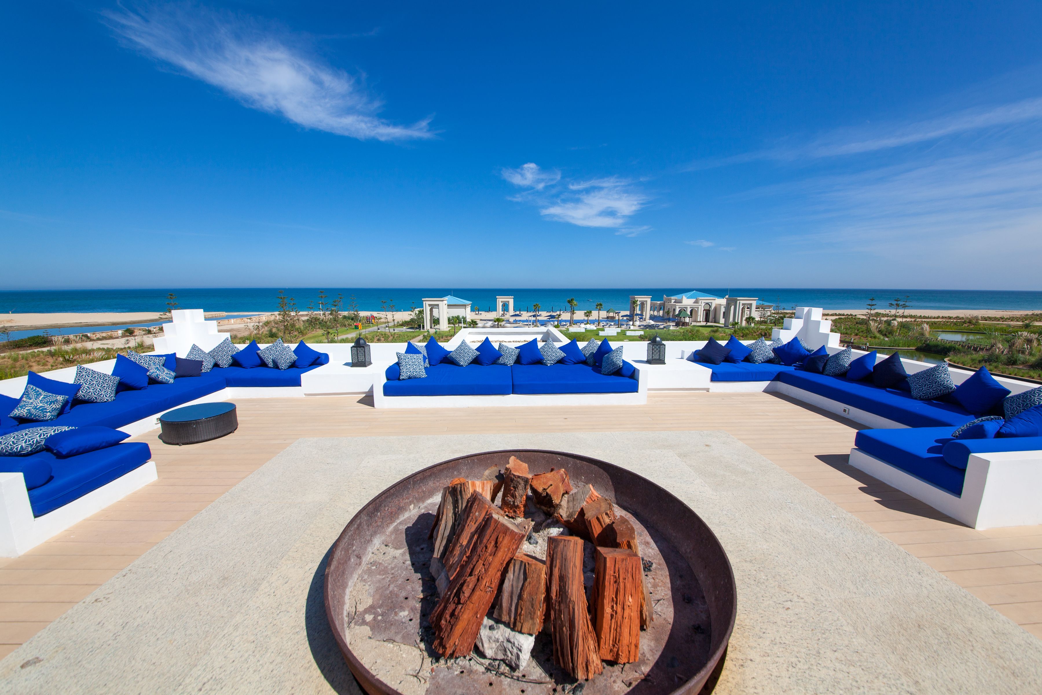 Una terraza en la azotea con asientos blancos y azules, una chimenea y vistas a la playa y el océano.