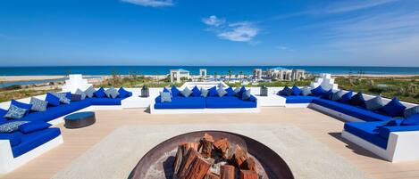 Una terraza en la azotea con asientos blancos y azules, una chimenea y vistas a la playa y el océano.