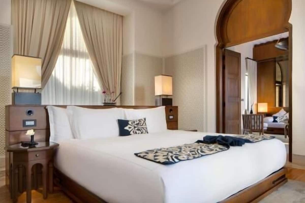 Ein Hotelzimmer mit einem großen Bett, zwei Nachttischen, einem Spiegel und einem Fenster mit Vorhängen.