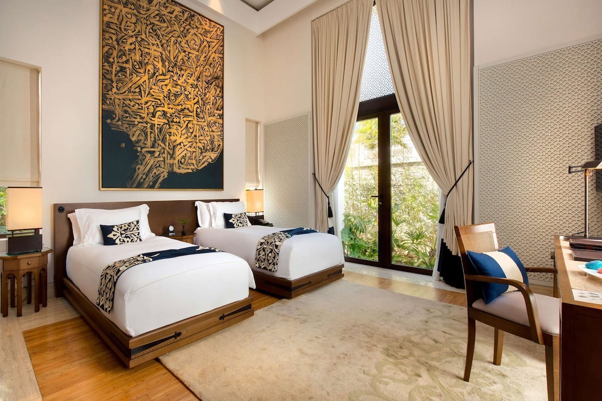 Ein Hotelzimmer mit zwei Betten, einem großen Kunstwerk an der Wand, einem Schreibtisch mit Stuhl und Blick auf Grünflächen.
