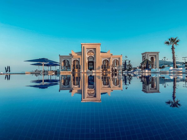 Un área de piscina lujosa con el reflejo de un edificio y palmeras.