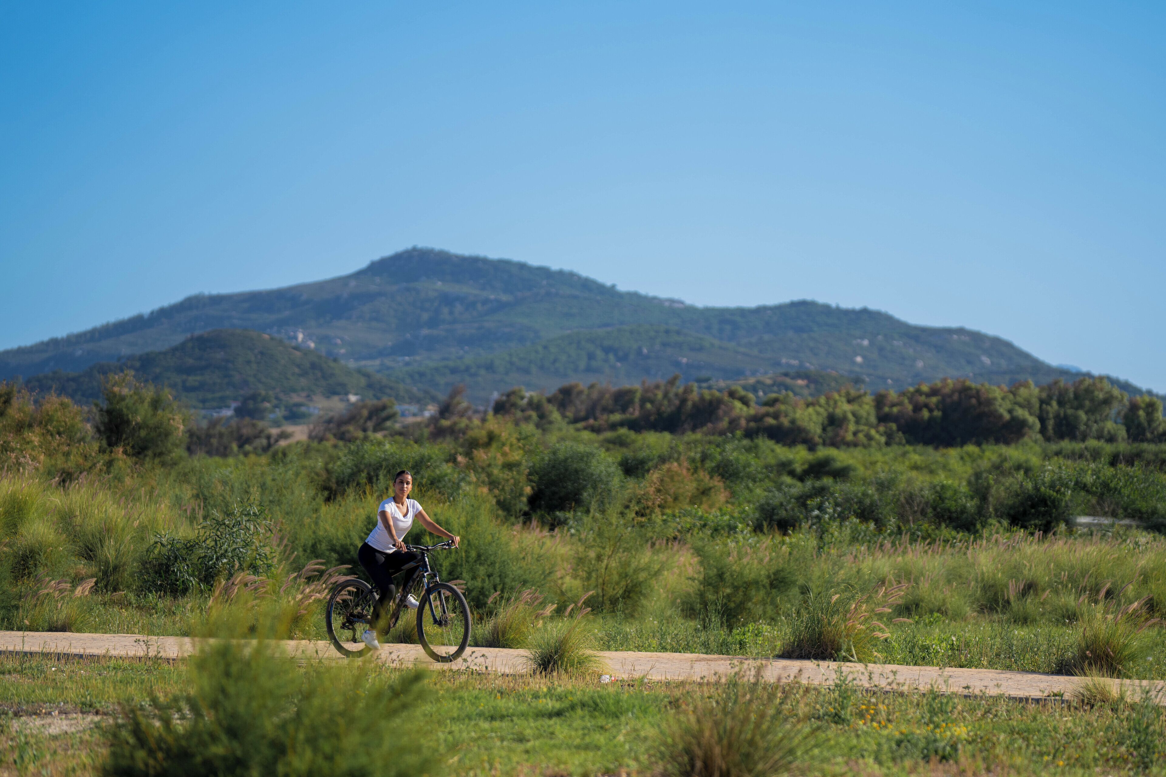 Una persona pedaleando en bicicleta por un sendero con una montaña al fondo.