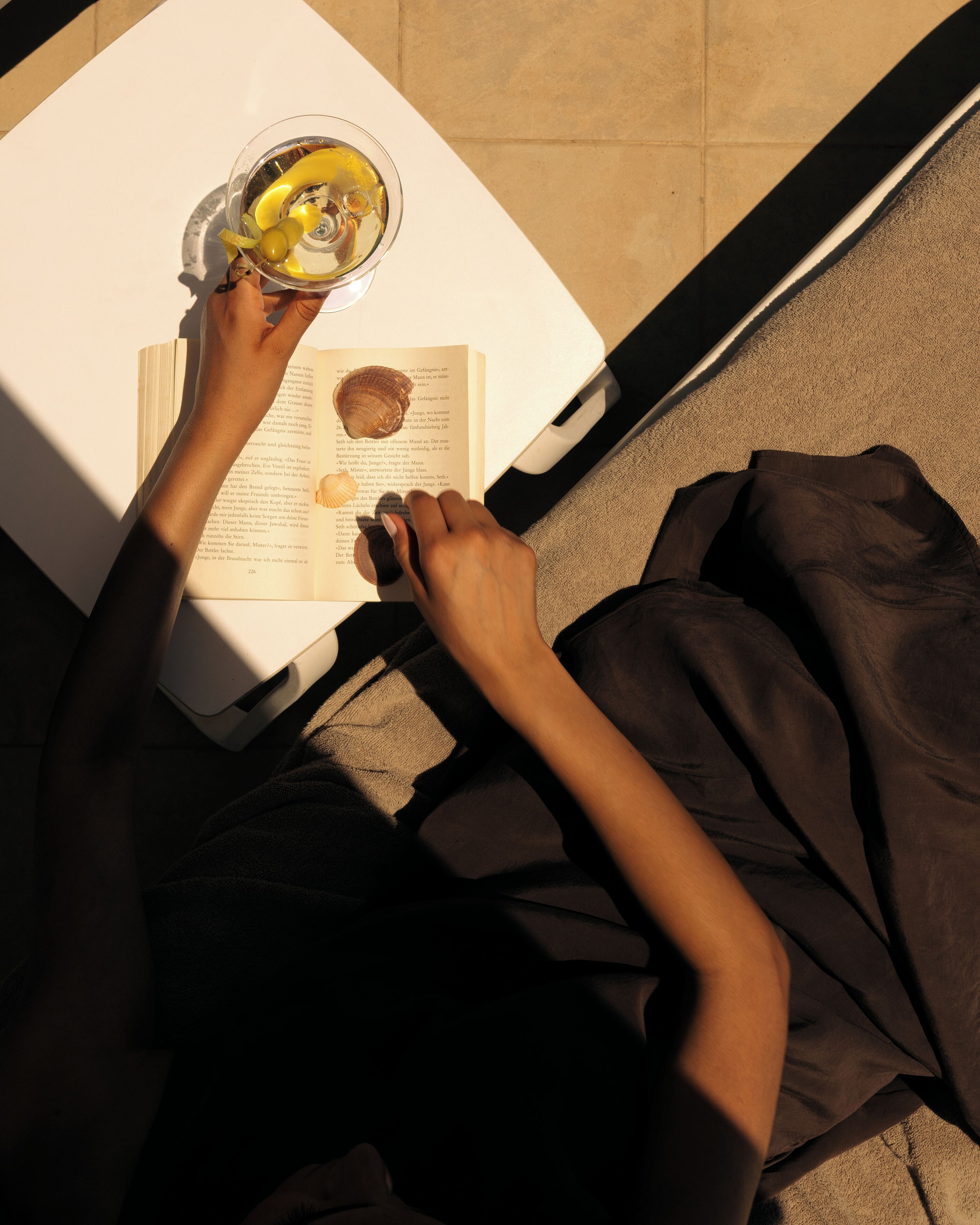 A person reading a book with a glass of wine on a white table.