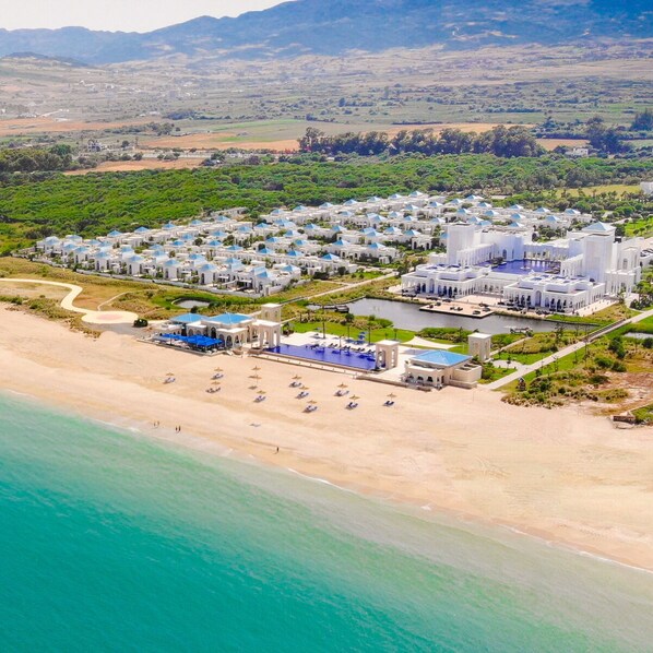 An aerial view of a coastal resort with multiple villas, a beach, and a pool area. - Banyan Tree Tamouda Bay (Allyene)
