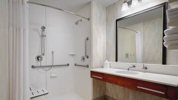 Un baño moderno con ducha a nivel, barras de apoyo, un espejo grande y un tocador con lavamanos y perchero.