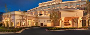 A large, well-lit hotel with a prominent 'Hyatt Place' sign, featuring a symmetrical facade, multiple windows, and a landscaped entrance area.