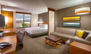 A hotel room with a bed, a sofa, a desk with a telephone, and a TV.