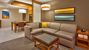 A modern hotel room with a sectional sofa, a small table, and a desk.