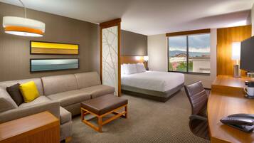 Habitación de hotel con cama, sofá, escritorio y vista a la ciudad.