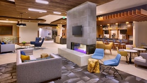 A modern lobby with a central fireplace, seating areas, and a bar.
