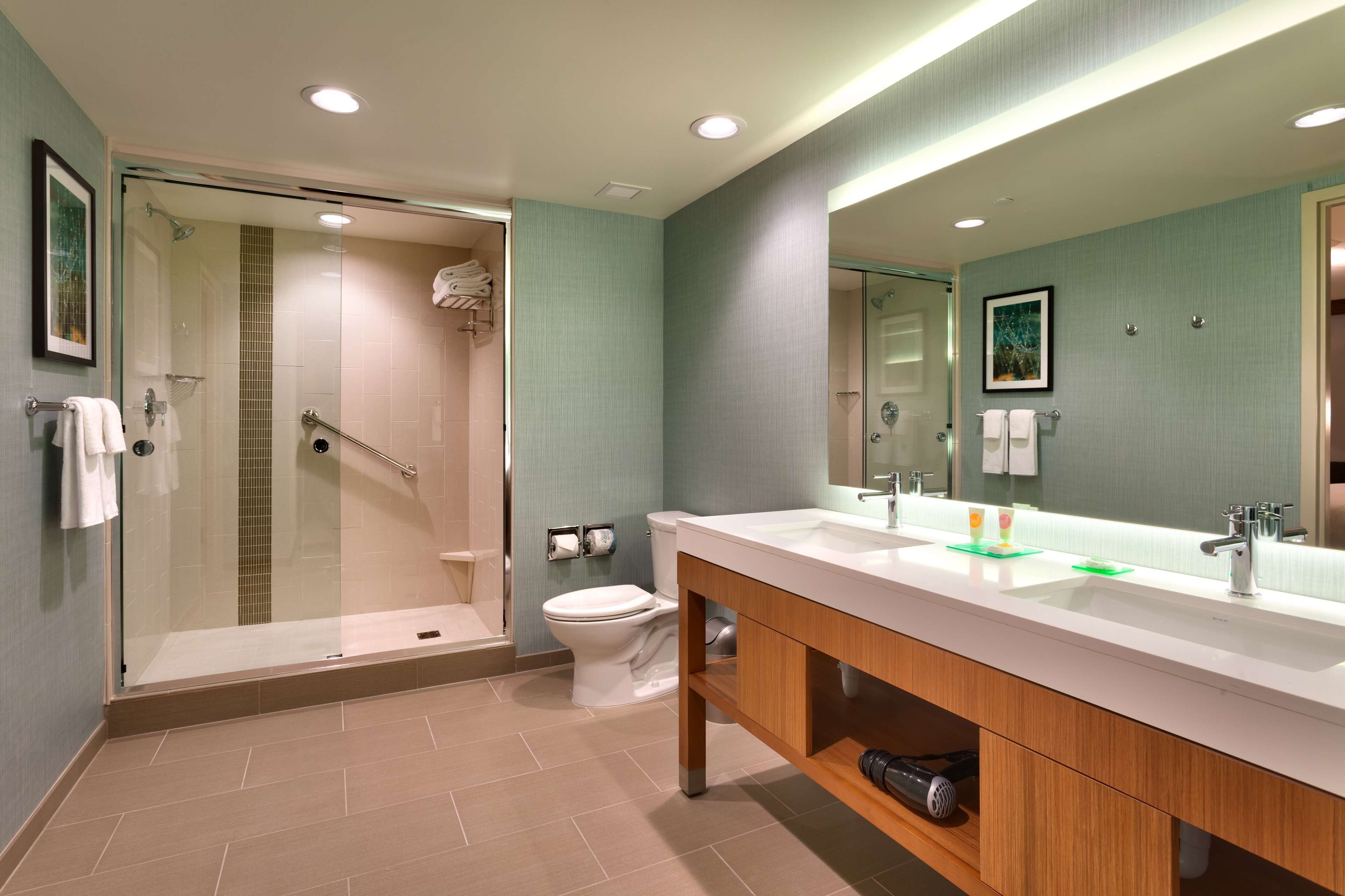 Un baño moderno con ducha de vidrio, lavamanos blanco y un espejo grande.