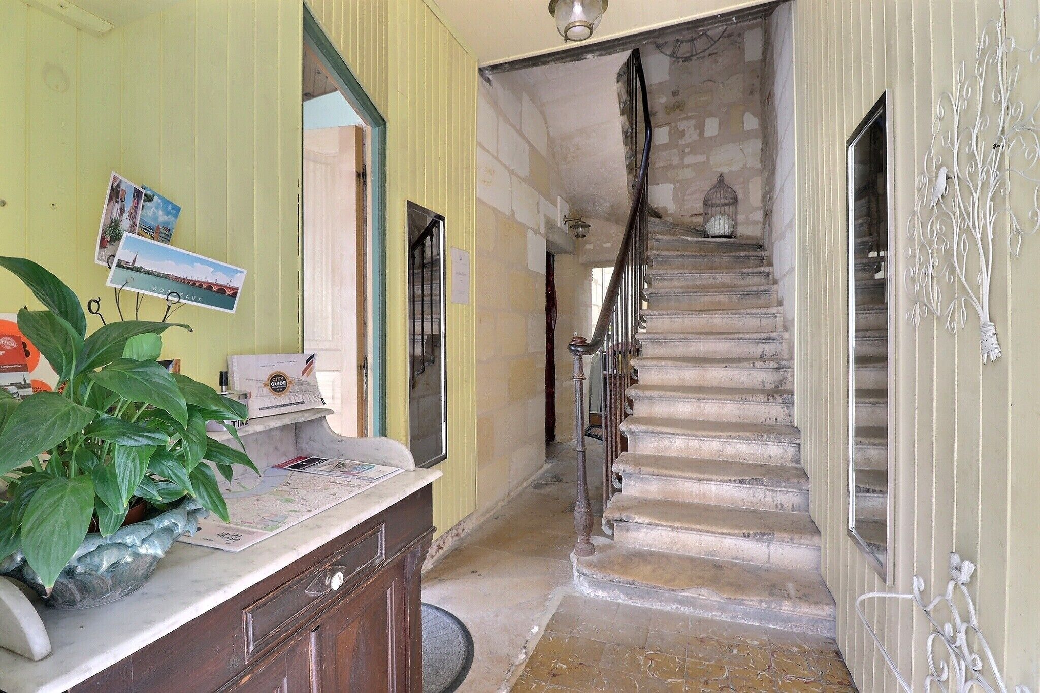 A hallway with a staircase, a reception desk with a plant, and a wall-mounted photo.