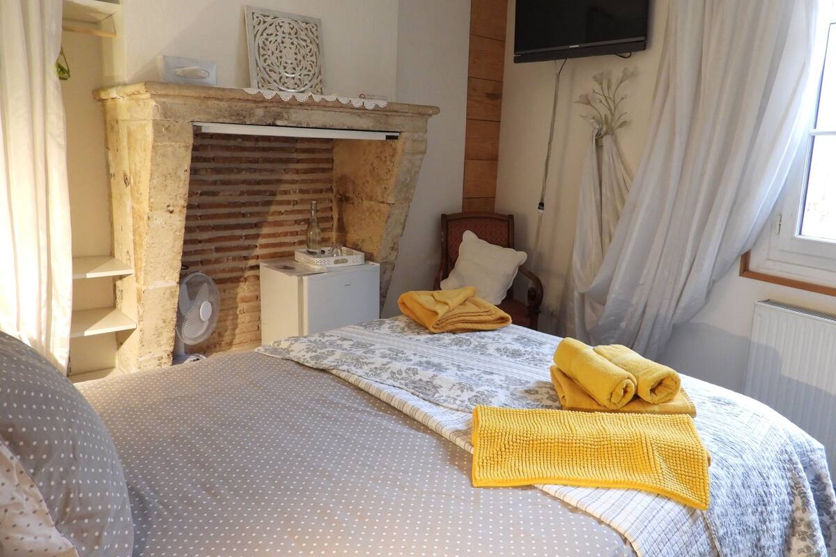 A bedroom with a stone fireplace, a bed with a polka dot bedspread, a wooden chair, and a TV mounted on the wall.