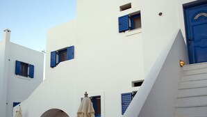 A white building with blue shutters, a blue door, and a staircase leading to the entrance. - Kanellis Studios (Kithira)