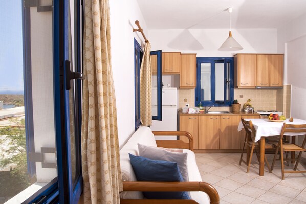 Une pièce comprenant un lit, une table à manger avec des chaises, un coin cuisine et donnant sur l’extérieur.