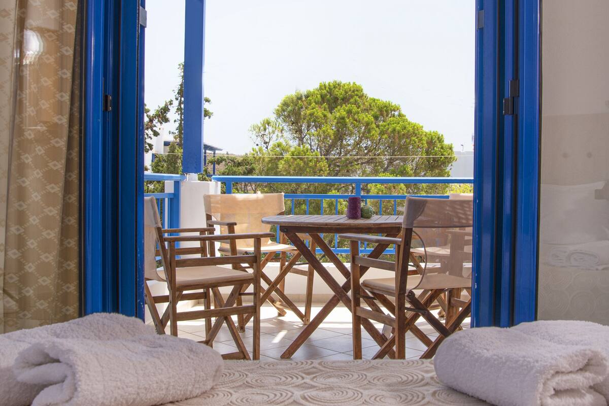 A room with a bed, a table, and chairs, and a view of the outdoors.
