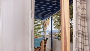 A bedroom with a bed, a view of a balcony with a table and chairs, and a wooden ceiling structure. - Kanellis Studios (Kithira)