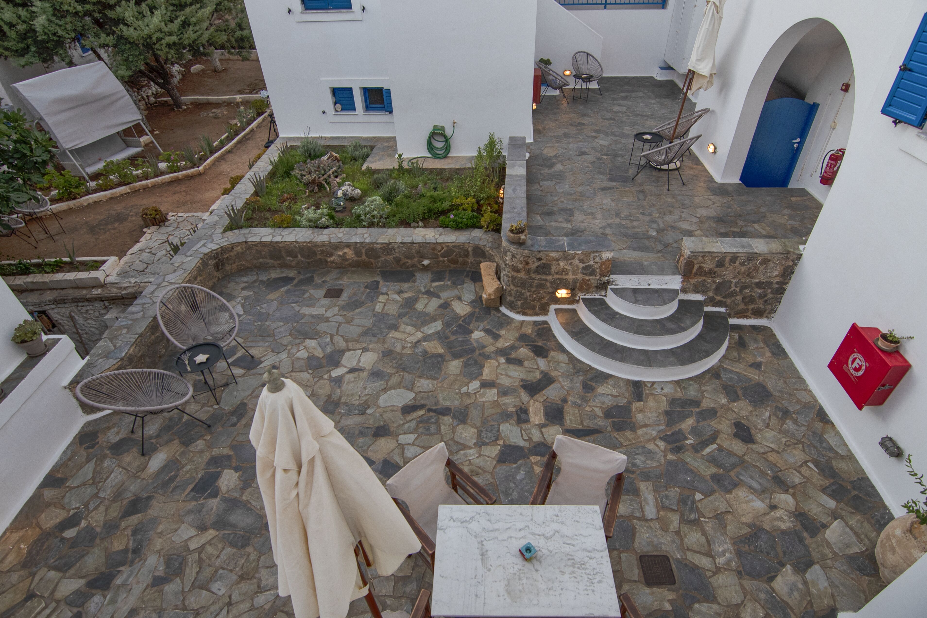 Un cortile con pavimento in pietra, arredi esterni, un tavolo bianco e un piccolo giardino.