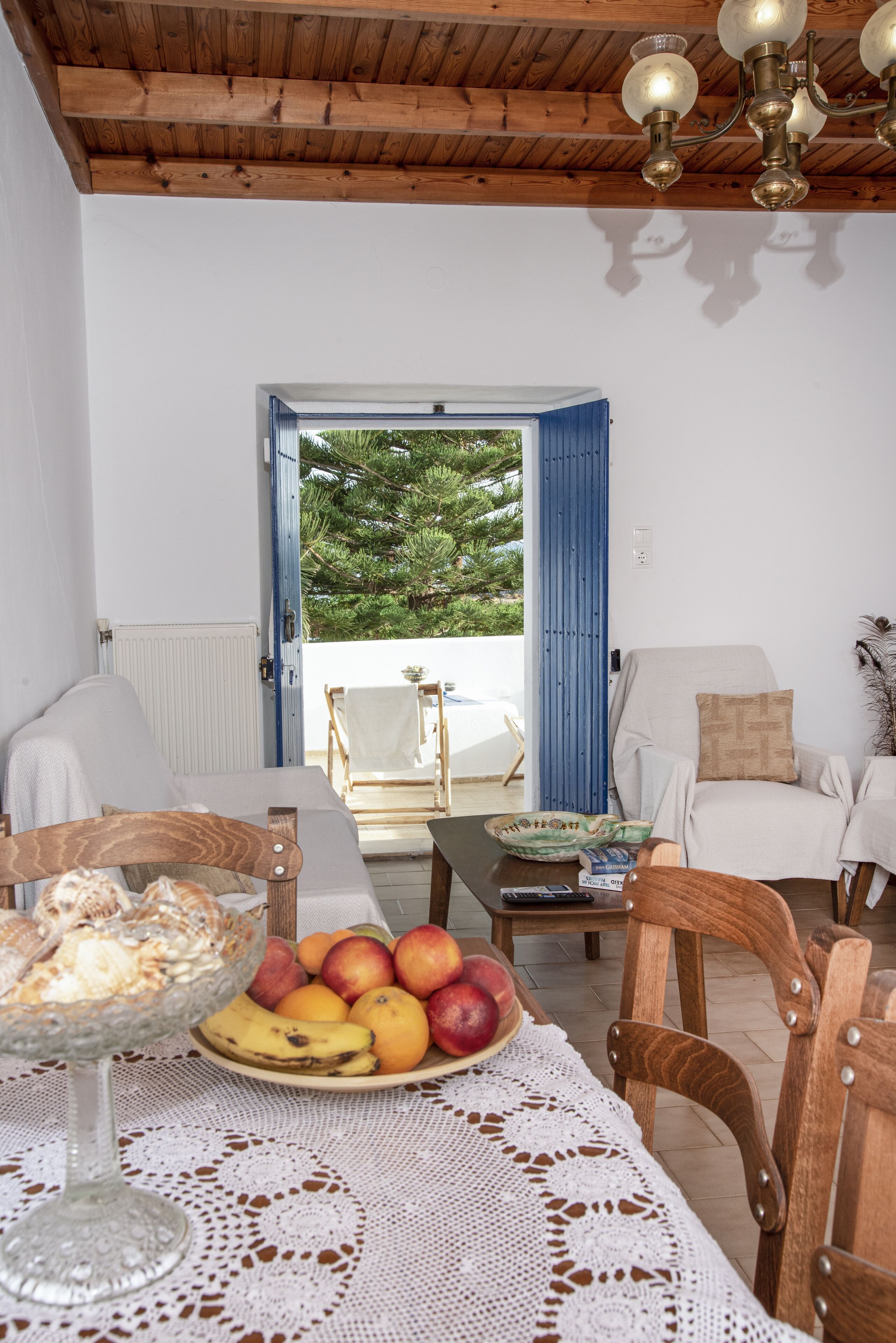 A cozy room with a wooden ceiling, a dining table with fruits, a bowl of cereal, and a view of the outdoors through an open door.