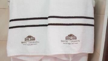 Una pila de toallas blancas con rayas negras y el logotipo del Hotel Colonial, colgadas en una pared con azulejos.