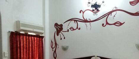A hotel room with two single beds, a wooden headboard, a red curtain, and a decorative wall design.