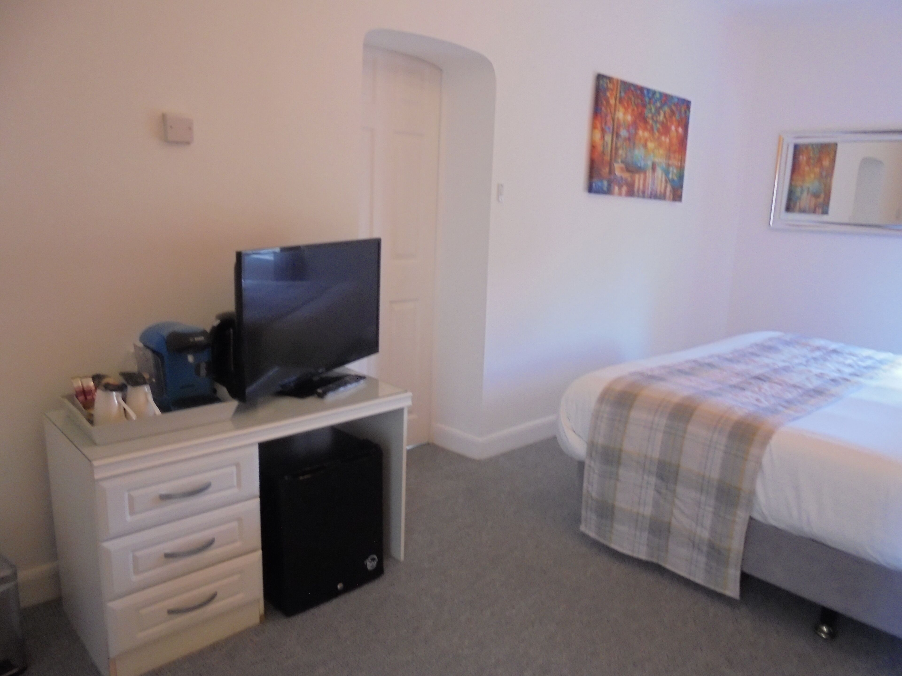 A bedroom with a bed, a television on a dresser, and a door.