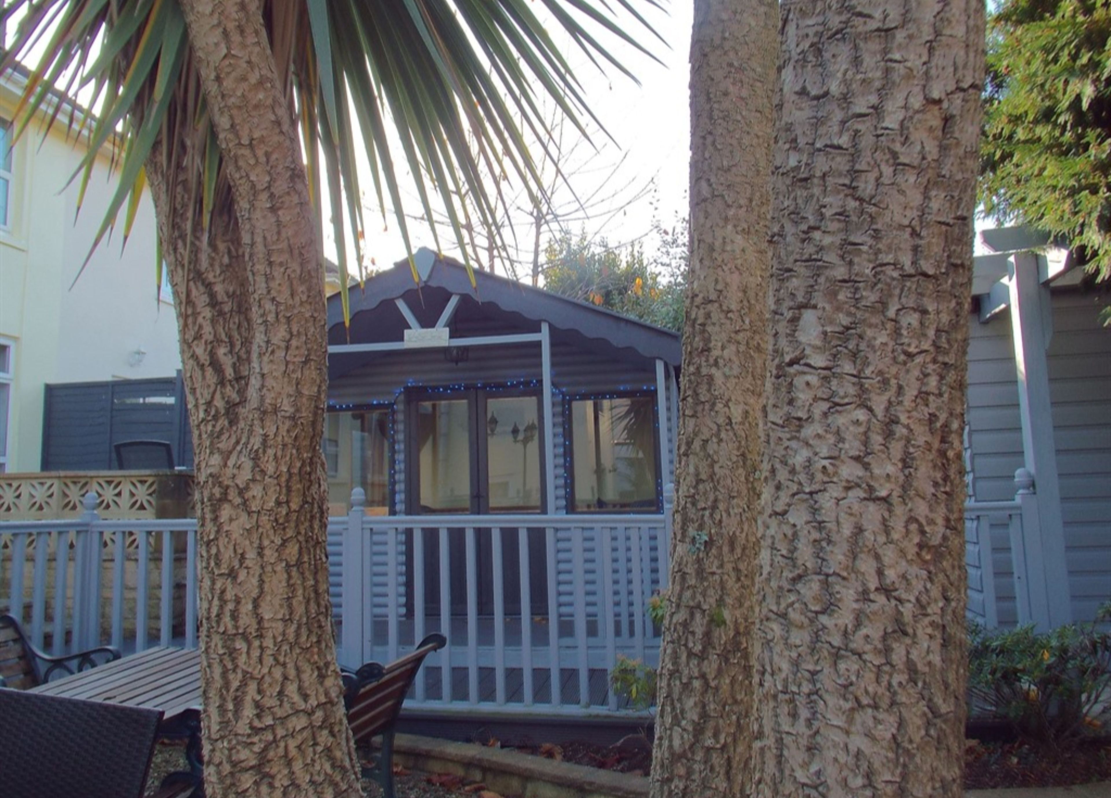 A covered outdoor seating area with a bench and a small table, surrounded by trees.