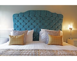 A bed with a tufted headboard, multiple pillows, and a bedside lamp.