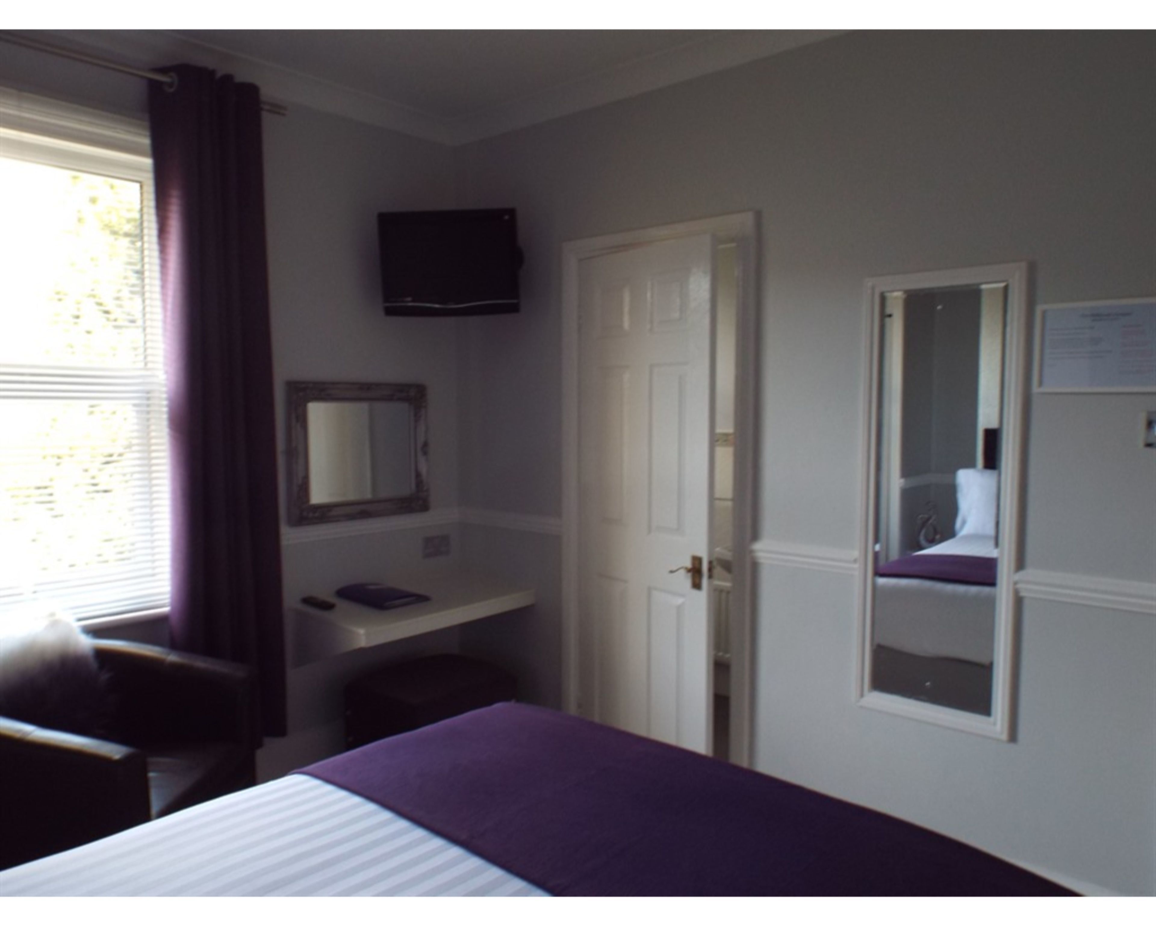 Un dormitorio con cama, escritorio, silla, televisor y puerta.
