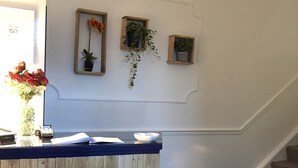 A reception desk with a wooden finish, a small potted plant, and a framed picture on the wall. - The Millbrook B & B (Torquay)